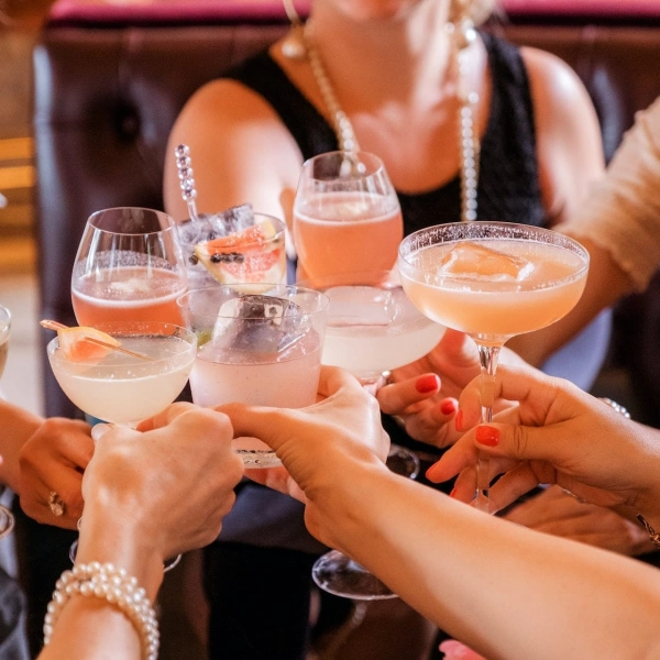 Plusieurs personnes trinquent avec des verres de cocktails variés aux couleurs pastel, dans une ambiance conviviale et élégante.