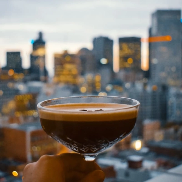 Verre à cocktail élégant rempli d'un espresso martini avec une vue floue sur une ville au crépuscule, évoquant une ambiance sophistiquée.