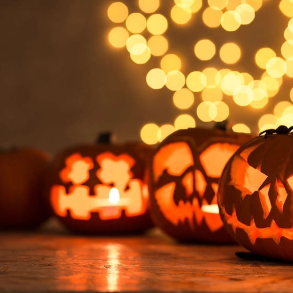 Citrouilles d'Halloween sculptées avec des visages effrayants et illuminées, devant des lumières floues en arrière-plan.