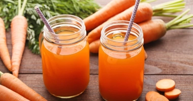 Verre de smoothie orange vif avec des carottes, une pomme verte et un morceau de gingembre frais sur une table en bois.