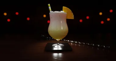 Cocktail Miami Vice avec une moitié blanche crémeuse et une moitié rouge fruitée, garni d'un quartier d'ananas et d'un petit parasol rose.