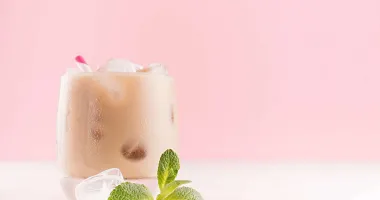 Verre à cocktail rempli de Midnight Mint crémeux avec une feuille de menthe verte décorative sur le dessus, posé sur une nappe beige avec des baies rouges en arrière-plan.