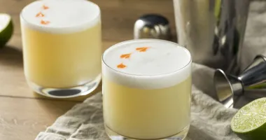 Verre à cocktail rempli de pisco sour, avec une mousse blanche onctueuse et quelques gouttes de bitters décorant le dessus.