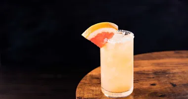 Un verre allongé rempli d'un cocktail rosé pâle avec de la glace pilée, garni d'une tranche de pamplemousse.