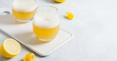 Un verre de Boston Sour garni d'un zeste de citron, avec une mousse blanche sur le dessus du cocktail.