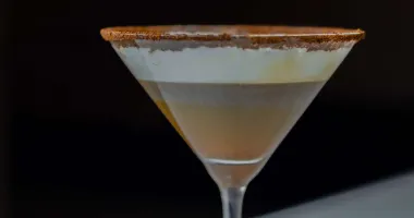 Un verre à cocktail rempli d'une boisson crémeuse de couleur beige, surmontée d'une légère pincée de cannelle en poudre.