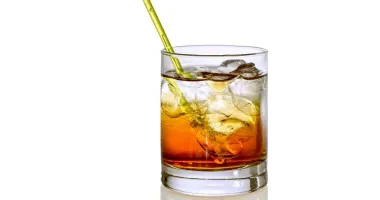 Un verre à whisky rempli de glaçons et d'un liquide ambré, posant sur une surface en ardoise, représentant un cocktail Godmother.
