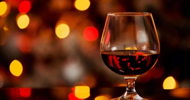 Verre à cognac rempli de cocktail ambré brillant sur fond de lumières floues rouges et oranges.
