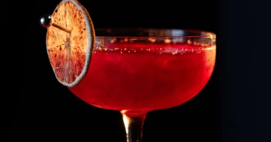 Verre à cocktail rempli d'un liquide rouge foncé surmonté d'un zeste d'orange.
