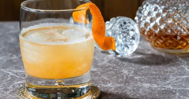 Verre à whisky avec un cocktail ambré, garni d'un zeste de citron.