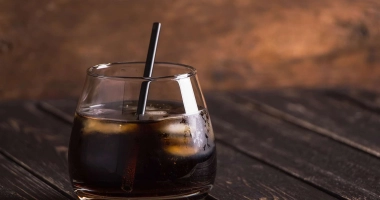 Verre de cocktail rempli de boisson sombre avec glaçons, accompagné de deux pailles rouges.