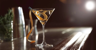 Verre à martini rempli de cocktail transparent avec des glaçons et une tranche de citron vert en garniture.
