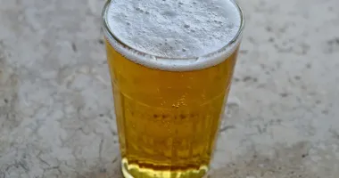 Verre à bière rempli d'un cocktail Radler jaune pâle avec une mousse crémeuse sur le dessus, posé sur une surface en pierre grise.