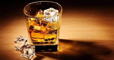 Un verre de whisky ambré rempli de glaçons, posé sur une table en bois éclairée par une lumière chaude.