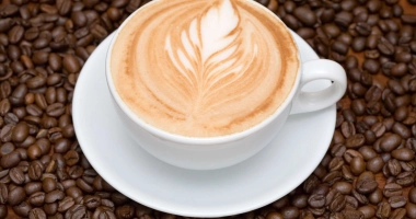 Une tasse de café chaud avec de la mousse crémeuse sur le dessus, entourée de grains de café éparpillés sur un fond de tissu en toile de jute.