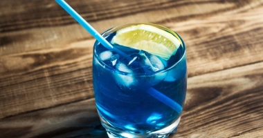 Un verre à cocktail rempli de liquide bleu vif, garni de glaçons et d'une tranche de citron sur le bord.