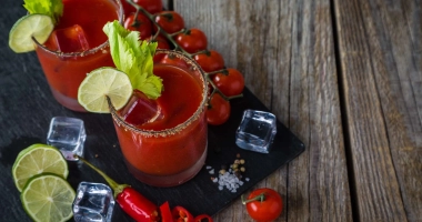 Verre de cocktail rempli de Tomato Tang, orné d'un quartier de citron vert et d'une paille rayée, avec un bord salé.