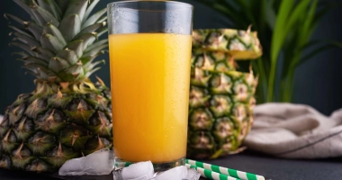 Deux verres de smoothie jaune vif à l'ananas, garnis d'un morceau d'ananas frais, posés sur une table en bois.