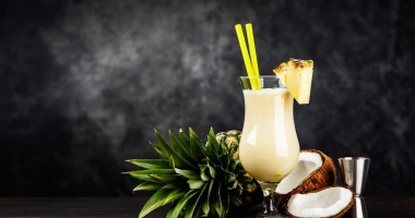Cocktail piña colada crémeux dans un verre ouragan, garni d'une tranche d'ananas, d'une cerise et d'un petit parasol rose.