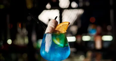 Verre à cocktail avec une boisson en dégradé de bleu au violet, garni de glaçons et une paille noire.