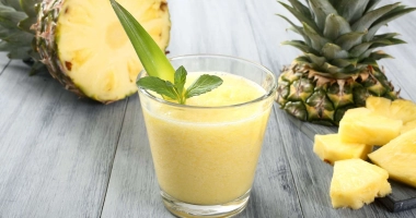 Deux verres de smoothie d'ananas, avec un morceau d'ananas frais décorant le bord du verre, sur une table en bois.