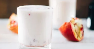 Trois verres de lassi, une boisson indienne crémeuse et mousseuse garnie de morceaux de pistache, sur une nappe foncée.