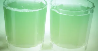 Un verre à shot transparent rempli d'un cocktail vert vif éclairé par une lumière douce.