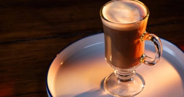 Cocktail Jamaican Coffee servi dans une tasse en verre avec une poignée, garni de crème fouettée et d'un bâtonnet de sucre.