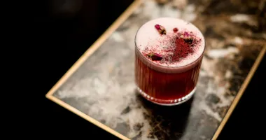 Verre de cocktail Pink Lady avec une garniture de fraise fraîche, rondelle d'ananas et spirale de zeste de citron.