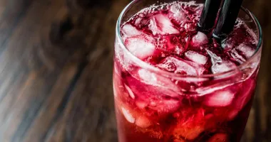Six verres de cocktail Alabama Slammer disposés en rangée, avec un dégradé de couleurs vives allant du rouge au jaune, garnis de tranches d'orange et de pailles noires.