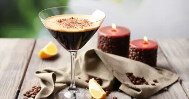 Un verre à martini contenant un cocktail espresso martini avec une mousse beige sur le dessus, décoré de trois grains de café.