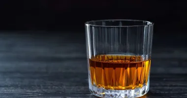 Un verre de cocktail carré rempli d'un liquide ambré posé sur une surface en bois.