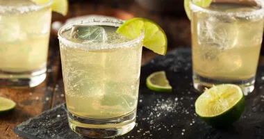 Un verre à cocktail rempli d'une margarita jaune pâle avec un bord glacé au sel et garni d'une tranche de citron vert.
