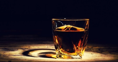 Un verre à whisky rempli de glaçons et de whisky ambré posé sur une surface en bois sombre.