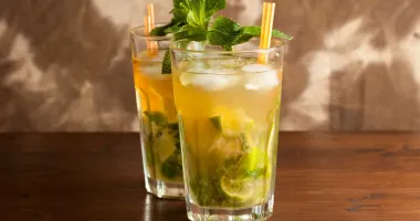Un verre à cocktail Bacardi rempli de Mojito lorrain, avec des feuilles de menthe fraîche et des tranches de citron vert, surmonté d'une paille noire.