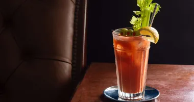 Cocktail Bloody Maria dans un verre à whisky garni d'une tige de céleri, avec une bouteille en arrière-plan.