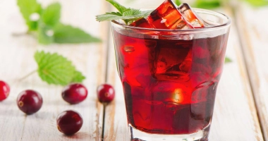 Un verre de cocktail « bleeding surgeon » avec des couches de couleurs rose vif et blanc, garni de glaçons translucides et un bâton à mélanger noir, tenu par une main.