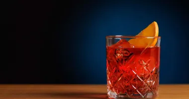 Un verre de Negroni sur fond noir, garni d'un zeste d'orange et contenant un gros glaçon.