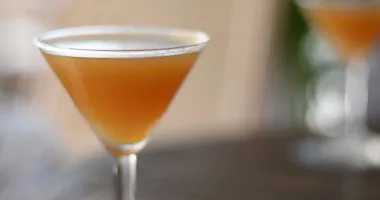 Cocktail ambré servi dans un verre à martini avec un sucre brun sur le bord.