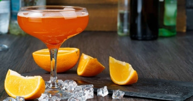 Verre à cocktail rempli d'un liquide ambré, garni d'une tranche d'orange.
