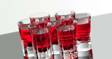 Trois verres à shot remplis d'un liquide rouge vif, disposés sur une surface noire brillante.
