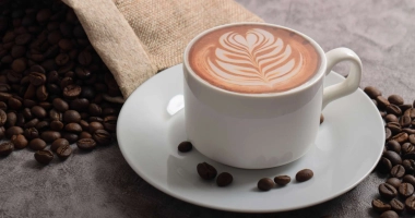 Tasse de café crémeux sur un tissu de jute, entourée de grains de café répartis autour.
