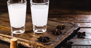 Verre à martini contenant un cocktail doré avec un zeste d'agrume, posé sur un comptoir en bois avec un arrière-plan flou de bouteilles et lumières tamisées.