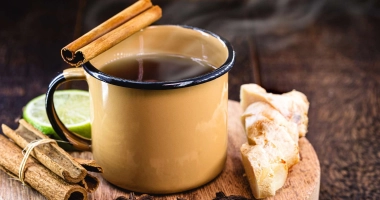 Tasse de masala chai servie chaude avec bâtons de réglisse noire en garniture, entourée d'épices entières comme la cardamome, le clou de girofle, la cannelle, l'anis étoilé et un quartier de citron.