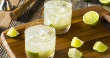 Un verre de Caipiroska avec des quartiers de citron vert, des glaçons et une paille transparente sur fond noir.