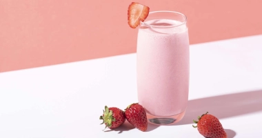 Un verre à cocktail contenant un smoothie crémeux, garni d'une fraise rouge et avec deux pailles colorées.