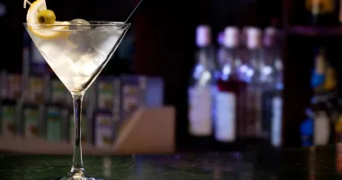 Un verre à martini transparent rempli d'un cocktail clair, garni d'une olive verte et accompagné d'un agitateur métallique.