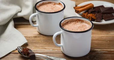 Une tasse de chocolat chaud crémeux servie dans une tasse blanche sur une soucoupe, avec des bulles à la surface de la boisson.