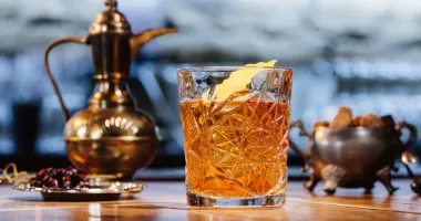 Verre à whisky rempli de cocktail ambré avec un gros glaçon, posé sur un plateau métallique.