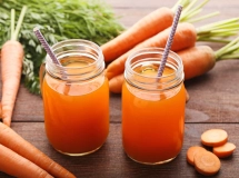 Verre de smoothie orange vif avec des carottes, une pomme verte et un morceau de gingembre frais sur une table en bois.